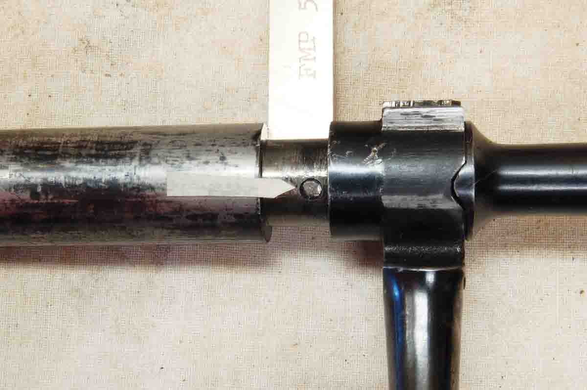 With the “key” removed, the bolt handle can move rearward exposing the pin (see arrow), which is driven out to complete disassembly, which may not be necessary.